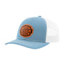 A light blue trucker-style cap with a white mesh back and a brown 'your design here' leather patch on the front panel, shown on a plain white background.