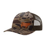 A trucker-style baseball cap with a brown and beige camouflage pattern on the front panel and brim, dark brown mesh back panels, and a brown cow leather patch on the front.
