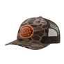 A camouflage trucker hat with a brown mesh back and a customizable brown patch on the front that reads 'YOUR DESIGN HERE'.