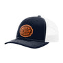 A navy blue trucker-style cap with a white mesh back and a brown 'your design here' leather patch on the front panel, shown on a plain white background.