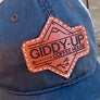 Blue cap with a brown leather patch featuring 'Giddy-Up Coffee House' on a wooden surface.