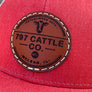Red cap with a circle brown leather patch featuring '797 Cattle Co.' on a wooden surface.