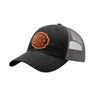 A black trucker-style cap with a grey mesh back and a brown 'your design here' leather patch on the front panel, shown on a plain white background.