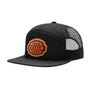 A black trucker-style cap with a flat brim, black mesh back panels, and a circular brown and brown embroidered patch on the front that reads 'YOUR DESIGN HERE'.