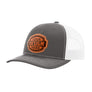 A grey trucker-style cap with a white mesh back and a brown 'your design here' leather patch on the front panel, shown on a plain white background.