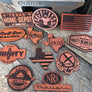 A collection of various shaped custom leather patches with different engravings, including text and logos.