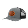 A heathered grey trucker-style cap with a black mesh back and a brown 'your design here' leather patch on the front panel, shown on a plain white background.