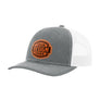 A heathered grey trucker-style cap with a white mesh back and a brown 'your design here' leather patch on the front panel, shown on a plain white background.