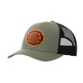 An olive green trucker-style cap with a black mesh back and a brown 'your design here' leather patch on the front panel, shown on a plain white background.