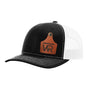 A black trucker style hat with a white mesh back, and a leather cattle tag shaped patch engraved with "wr" on a white background
