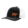 A black trucker hat with a white mesh back, and a brown cow leather patch on the front panel, shown against a plain white background.