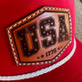 Red cap with a leather patch featuring 'USA 1776' on a wooden surface